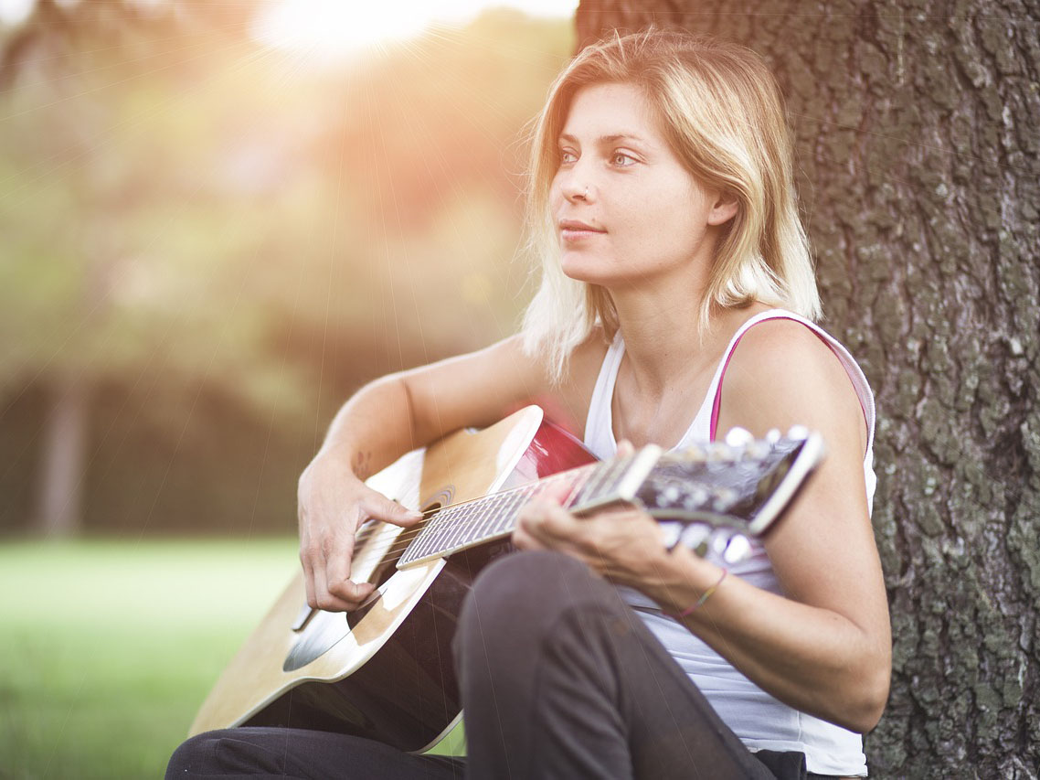 Eine junge frau sitzt mit ihrer Gitarre im Freien und macht Musik. (c) Foto: Pixabay